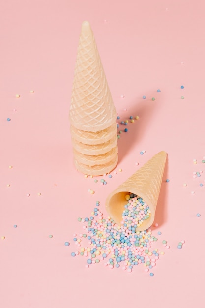 Free photo party sprinkles balls spilling from waffle cone against pink background