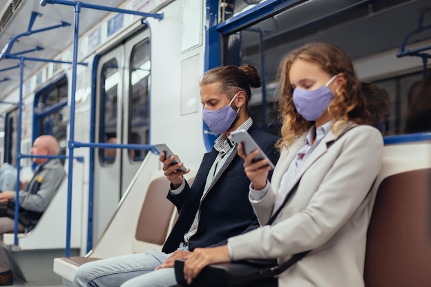 마스크를 쓴 승객들이 지하철에 앉아 스마트폰을 사용하고 있다. 건강 보호의 개념입니다.