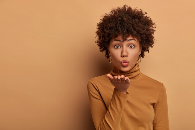 Passionate good looking woman with Afro hairstyle blows airkiss