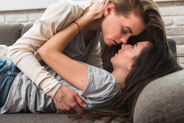 Passionate lesbian young couple loving each other on grey sofa