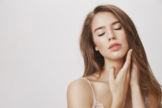 Passionate woman with closed eyes touching face gently