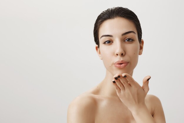 Passionated woman standing with naked shoulders and sending air kiss at front