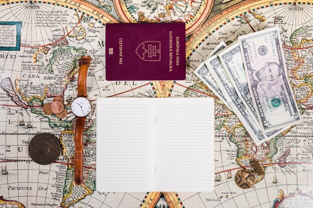 Passport, banknotes, wristwatch, coins and notepad on map
