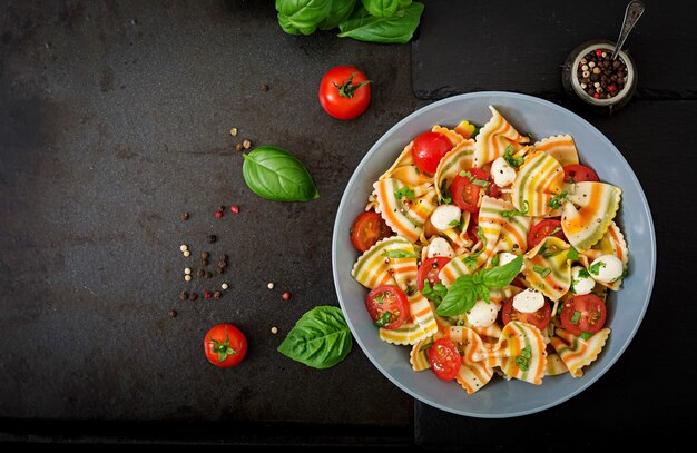Pasta colored farfalle salad with tomatoes, mozzarella and basil.