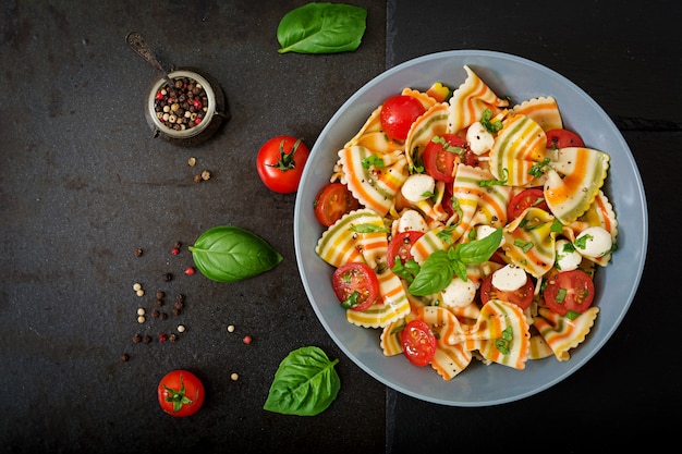 Pasta colored farfalle salad with tomatoes, mozzarella and basil.