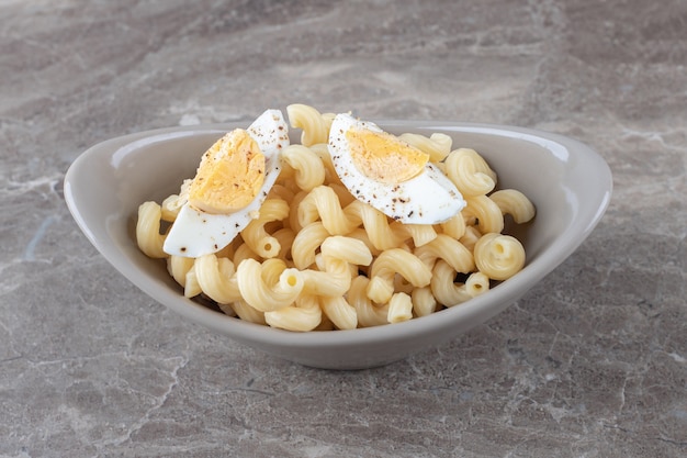 Pasta decorated with boiled egg in ceramic bowl. 