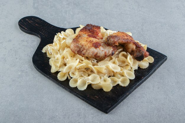 Pasta and grilled chicken on black board.