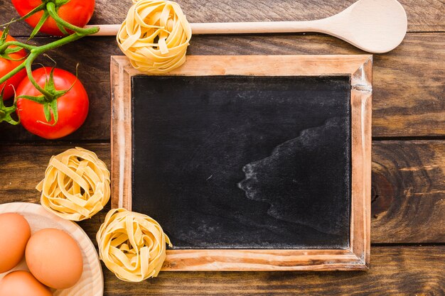 Pasta ingredients and spoon near blackboard