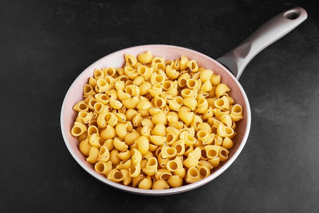 Pasta isolated on black in a pink skillet.