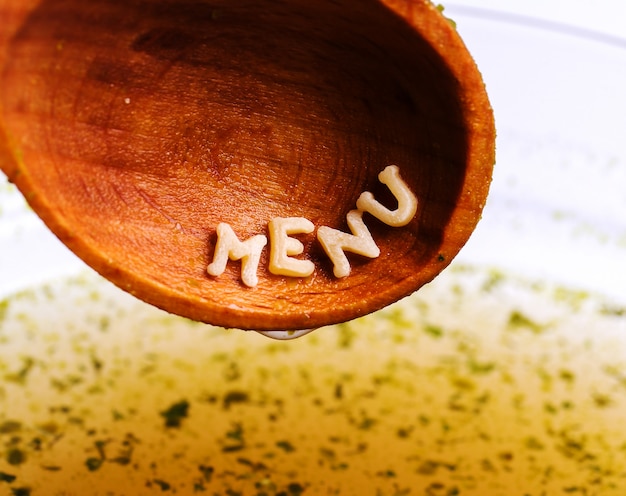 Free photo pasta letters with menu word on wooden spoon