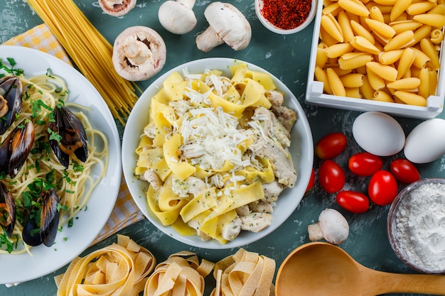 Pasta meals in plates with raw pasta, tomato, flour, mushroom, eggs, spice, spoon