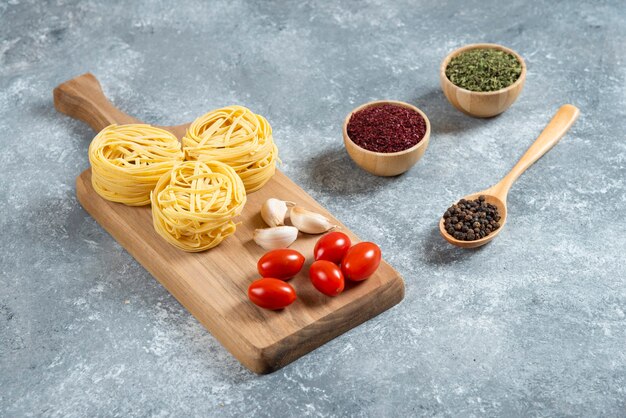 Pasta nests, garlic and cherry tomatoes on wooden board.