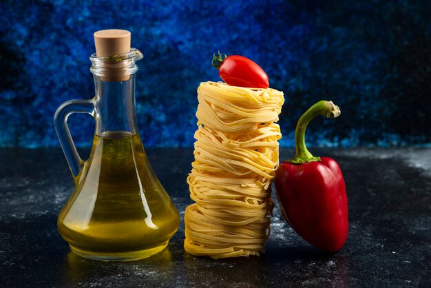 Pasta nests, oil and vegetables on marble table.