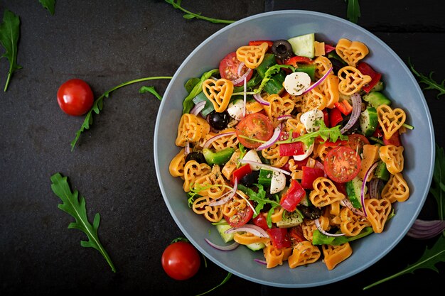 Pasta in the shape heart salad with tomatoes, cucumbers, olives, mozzarella and red onion Greek style. Flat lay. Top view