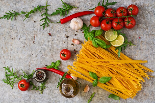 Pasta Tagliatelle and ingredients for cooking (tomatoes, garlic, basil, chili). Top view