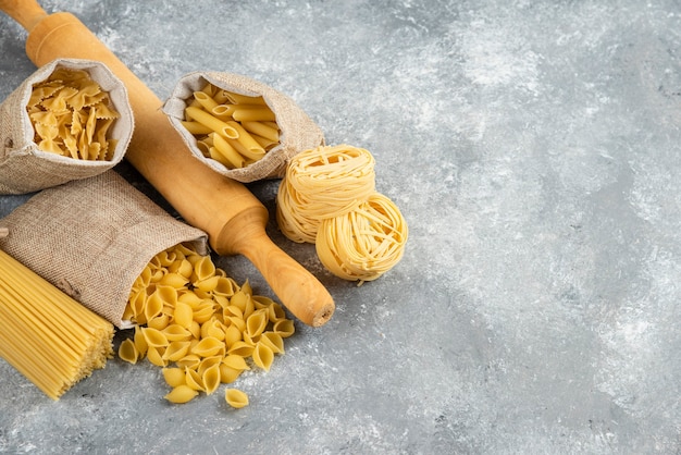 Pasta varieties in rustic basket with a wooden rolling pink on marble table.