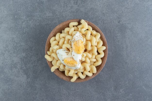Pasta with boiled eggs in wooden bowl.