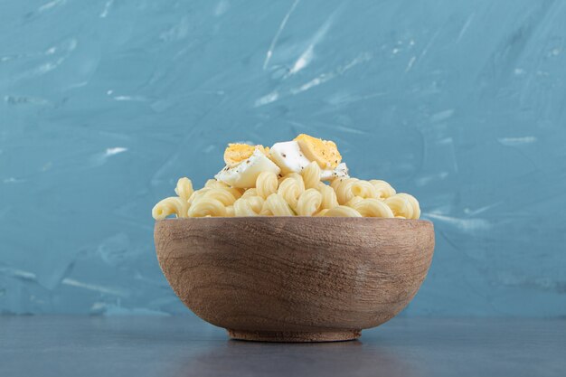 Pasta with boiled eggs in wooden bowl.