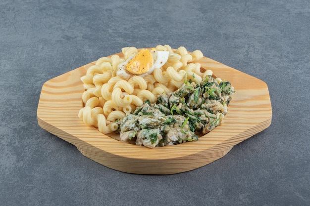 Pasta with delicious eggs on wooden plate.