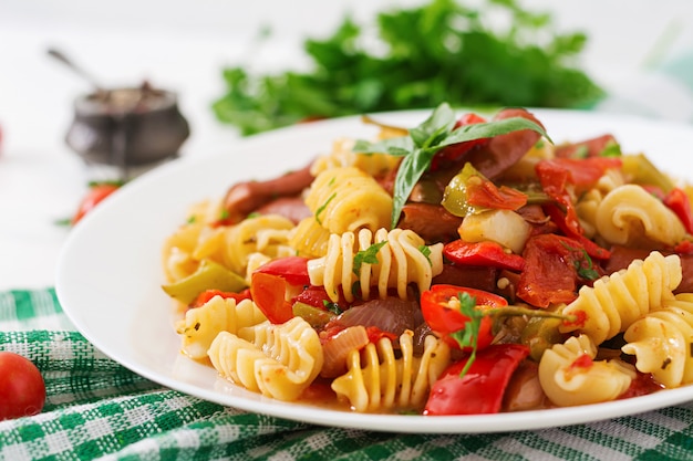 Pasta with tomato sauce with sausage, tomatoes, green basil decorated in white plate on a wooden table.