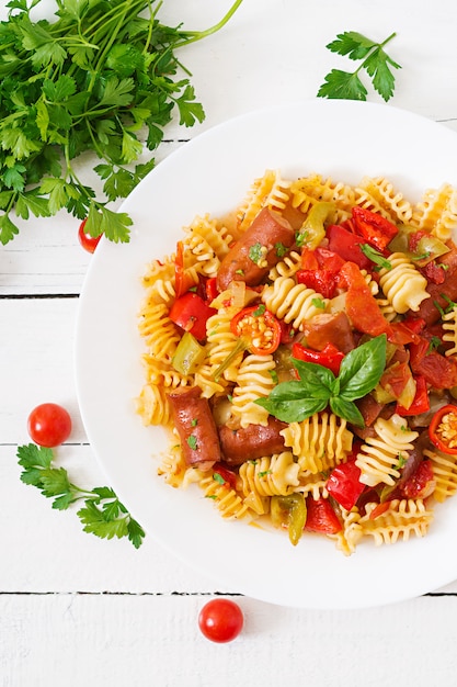 Pasta with tomato sauce with sausage, tomatoes, green basil decorated in white plate on a wooden table. 