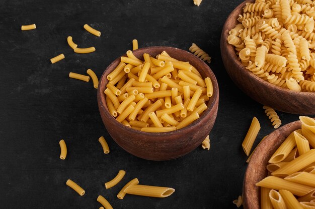 Pasta in wooden cups on black surface. 