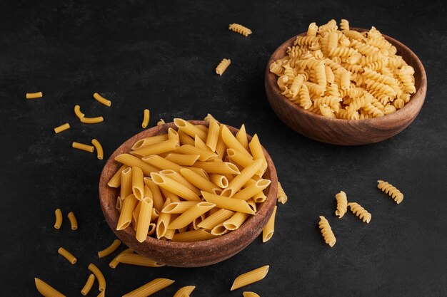 Pasta in wooden cups on black surface. 
