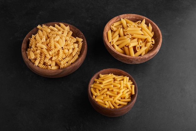 Pasta in wooden cups in the center on black surface.