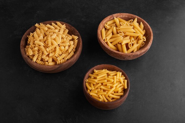 Pasta in wooden cups in the center on black surface.