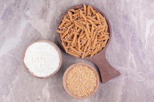 Pasta on a wooden platter with wheat and blended flour in cups