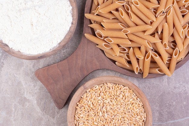 Pasta on a wooden platter with wheat and flour in wooden cups. 