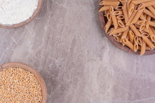 Pasta on a wooden platter with wheat and flour in wooden cups. 