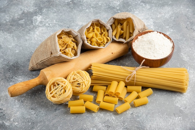 Pastas in rustic basket with rolling pin and a wooden cup of flour around.