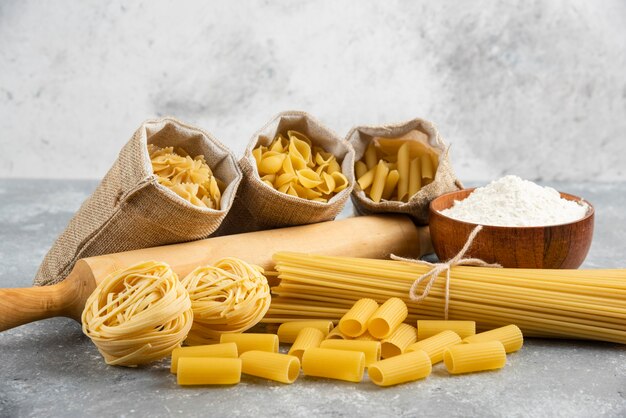 Pastas in rustic basket with rolling pin and a wooden cup of flour around.