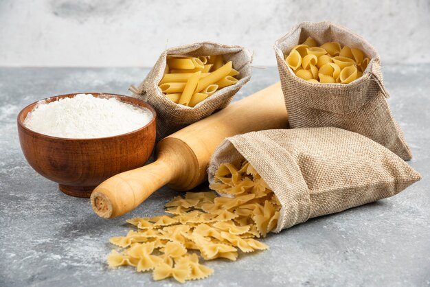 Pastas in rustic basket with rolling pin and a wooden cup of flour around.