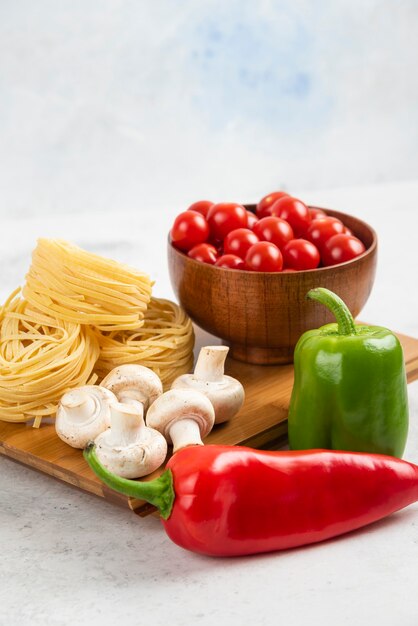 Pastas with mushrooms, chili peppers and cherry tomatoes on a wooden board.