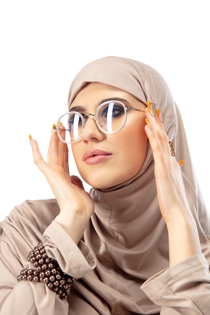 파스텔. 아름 다운 아랍 여자와 벽에 고립 된 세련 된 hijab에서 포즈. 패션, 뷰티, 스타일 개념. 트렌디 한 메이크업, 매니큐어 및 액세서리가있는 여성 모델.