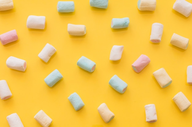 Free photo pastel colored marshmallow on yellow background