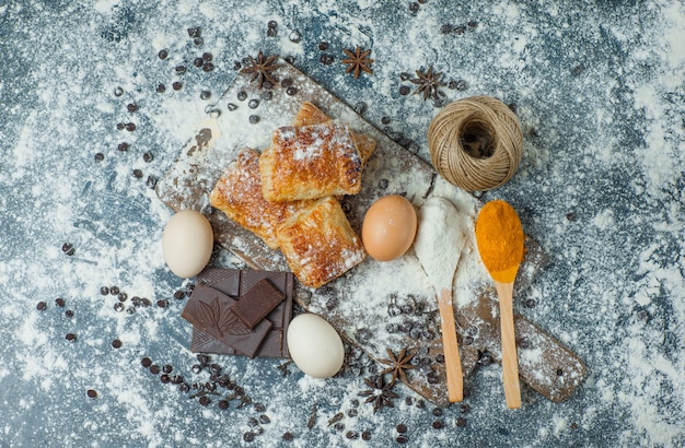 Pastries with flour, chocolate, spices, eggs, thread on concrete and cutting board, top view.