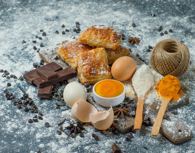 Pastries with flour, chocolate, spices, eggs, thread high angle view on concrete and cutting board