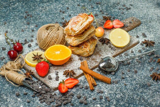 Pastries with flour, fruits, choco chips, spices, thread ball high angle view on stucco and cutting board