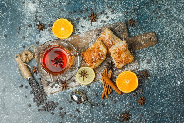 Pastries with flour, tea, orange, choco chips, spices top view on stucco and cutting board
