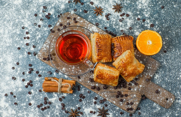 Free photo pastries with tea, flour, choco chips, spices, orange on concrete and cutting board, top view.