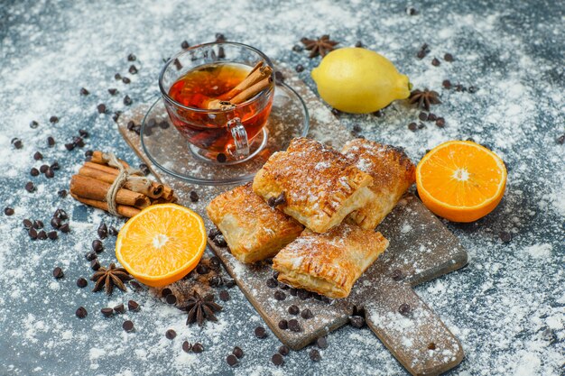Pastries with tea, flour, choco chips, spices, orange, lemon on concrete and cutting board