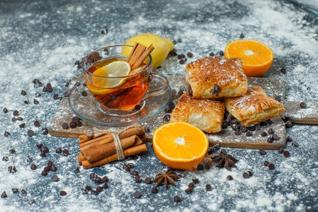 Pastries with tea, flour, choco chips, spices, orange, lemon high angle view on concrete and cutting board