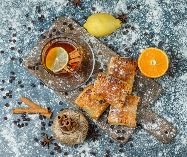 Pastries with tea, flour, choco chips, thread, spices, orange, lemon on concrete and cutting board