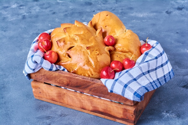 Pastry bun with cherries on a wooden board on blue