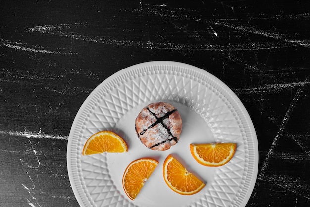 A pastry bun with chocolate syrup served with orange slices.