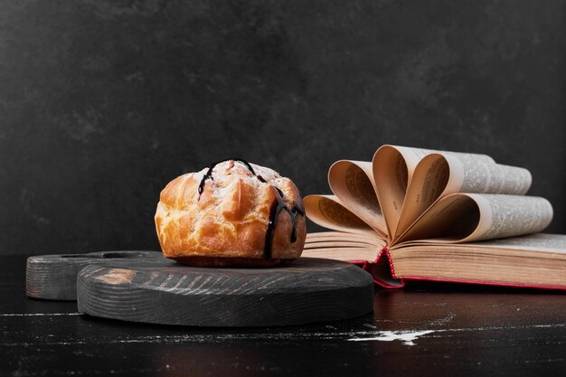 A pastry bun with chocolate syrup on a wooden board.