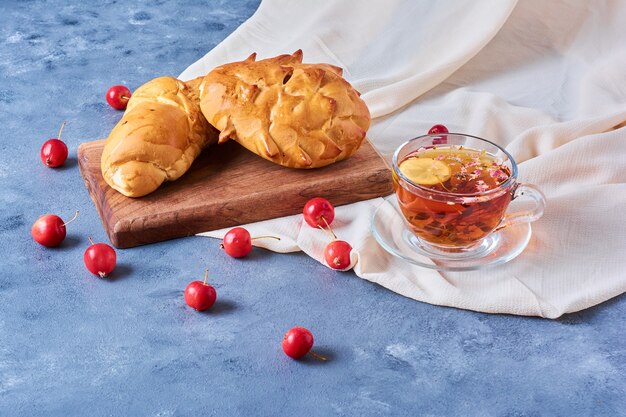 Pastry bun with a cup of tea on a wooden board on blue